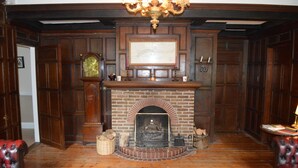 A room with a brick fireplace, wooden paneling, a chandelier, and leather armchairs. - Pwll-y-Faedda (Builth Wells)