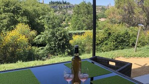 Une table avec une bouteille et des verres, entourée de verdure et offrant une vue sur des arbres et des collines.