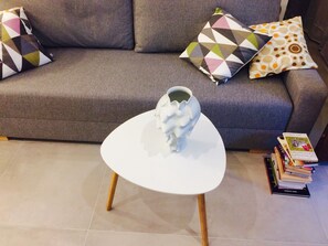 A living room with a grey sofa, patterned cushions, a white coffee table with a white sculpture, and a stack of books. - Piper Cytadela Apartament (Poznan)