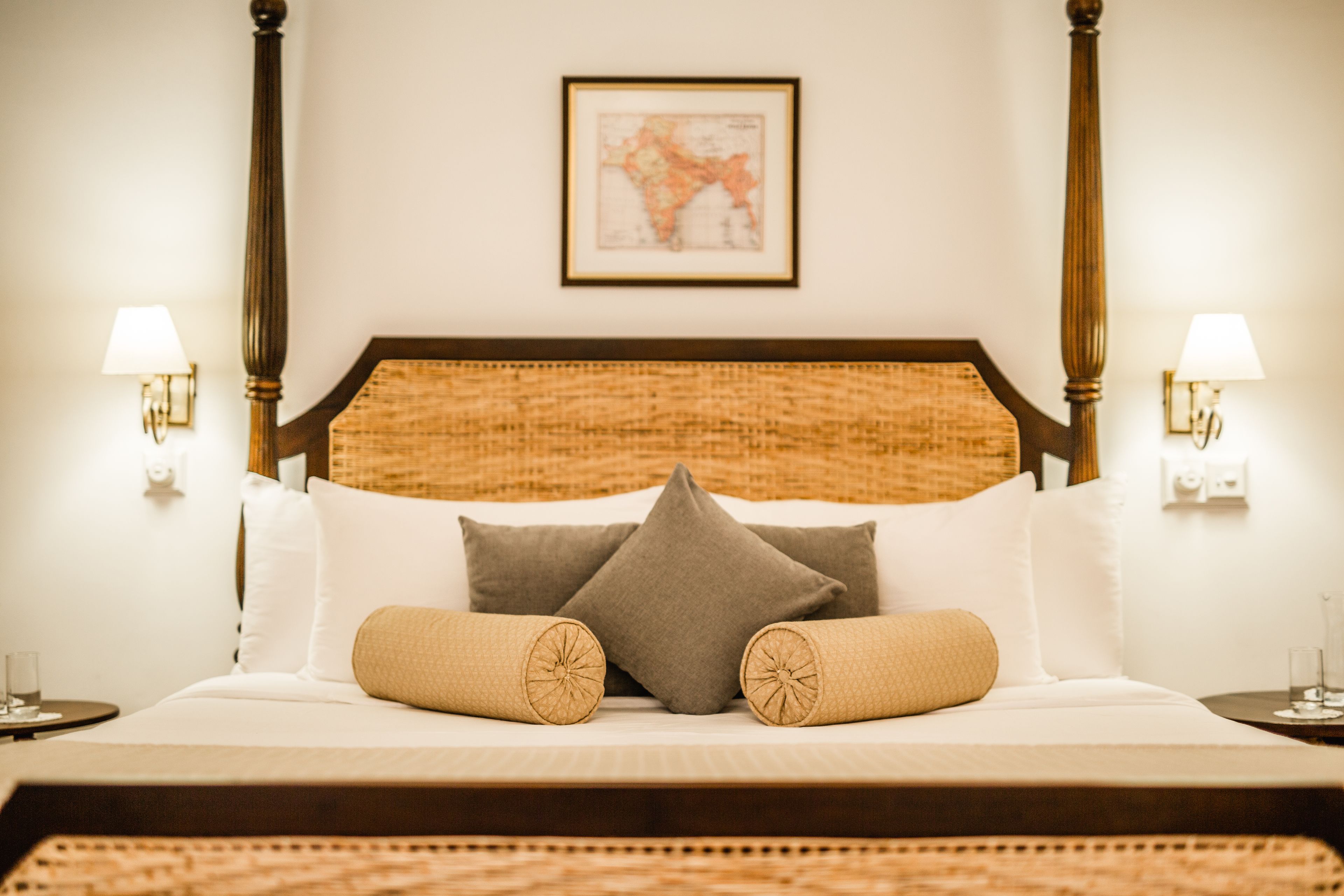 A bed with a wooden headboard, two wall-mounted lamps, and a framed map on the wall.