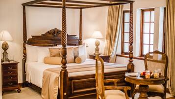 A four-poster bed with a wooden frame, a bedside table with a lamp, and a chair with a table beside it.