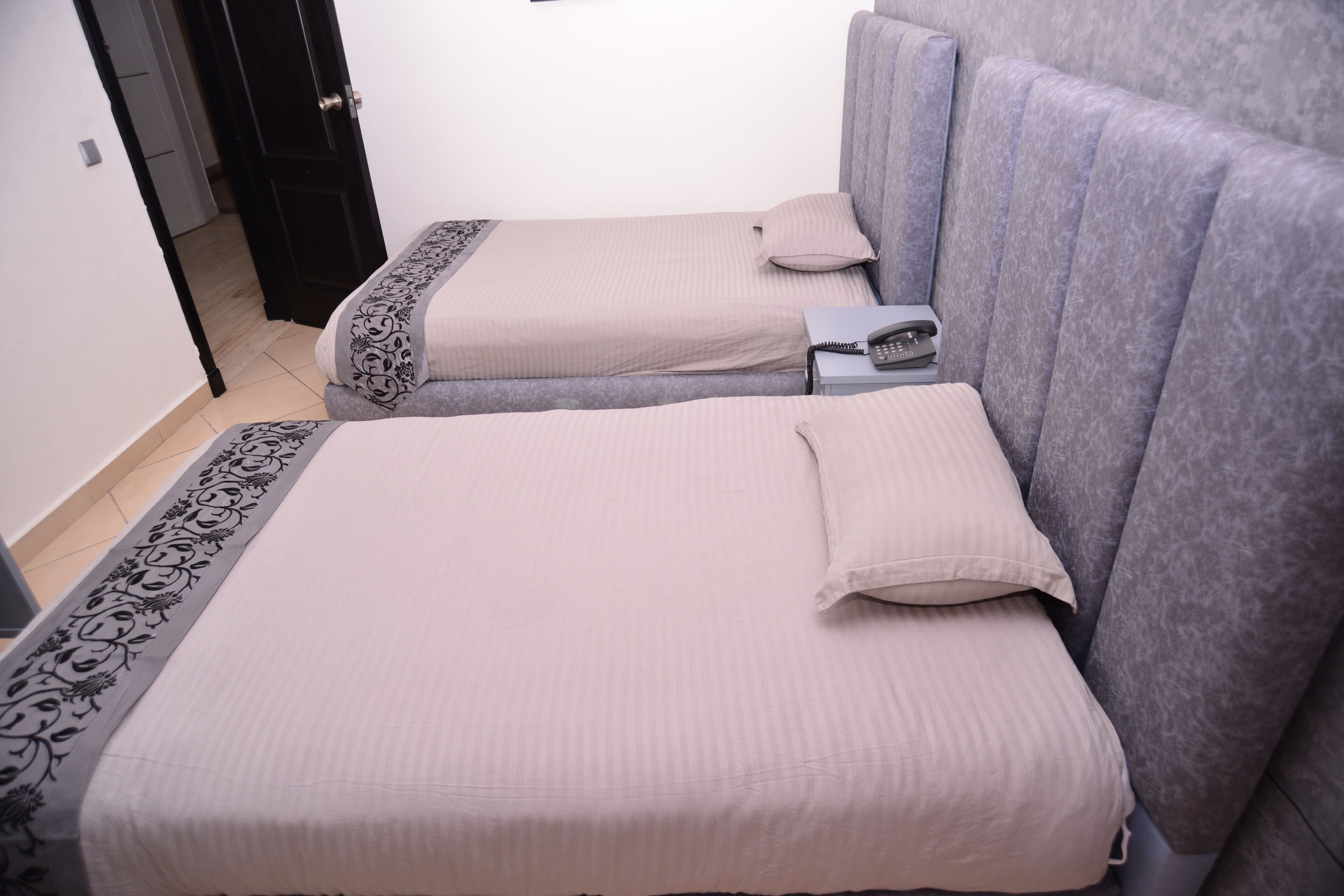 Two single beds with headboards, a bedside table with a phone, and a door leading to another room.