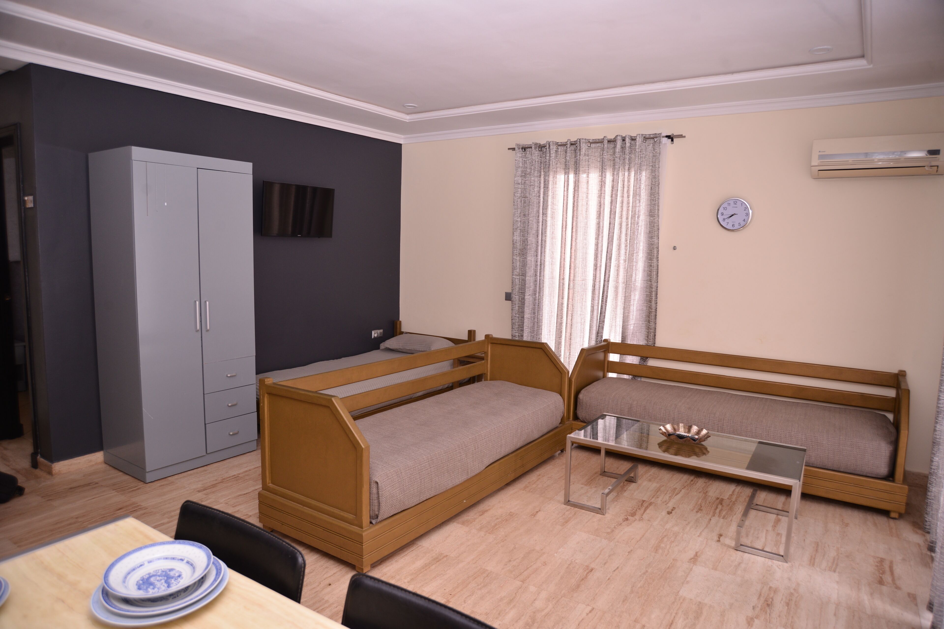 A room with a bunk bed, a desk with a chair, a wardrobe, a television, and an air conditioning unit.