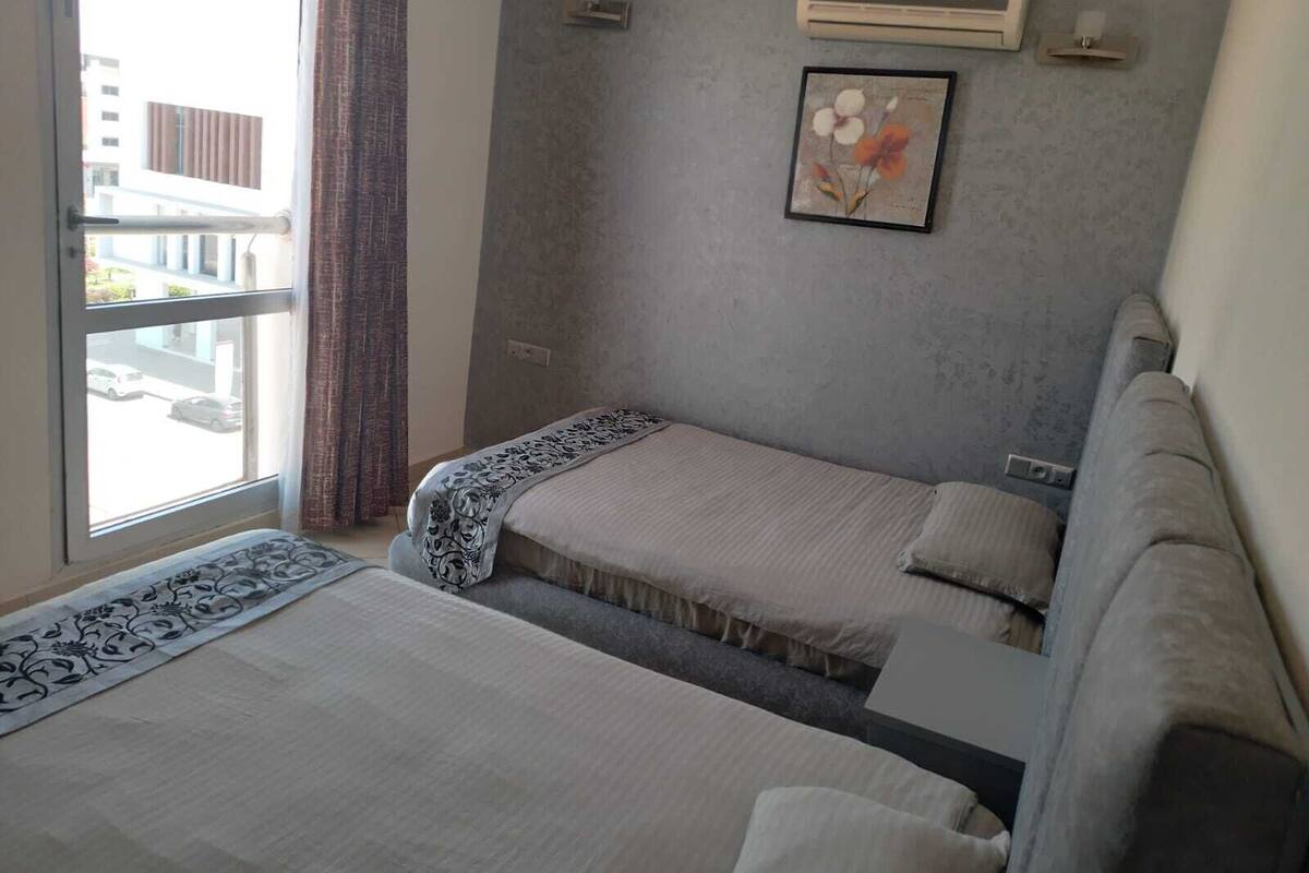 Een hotelkamer met twee bedden, een raam met uitzicht op de straat en een luchtverkoeler aan de muur.