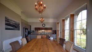 Un comedor espacioso con una gran mesa de madera, sillas tapizadas y un candelabro.