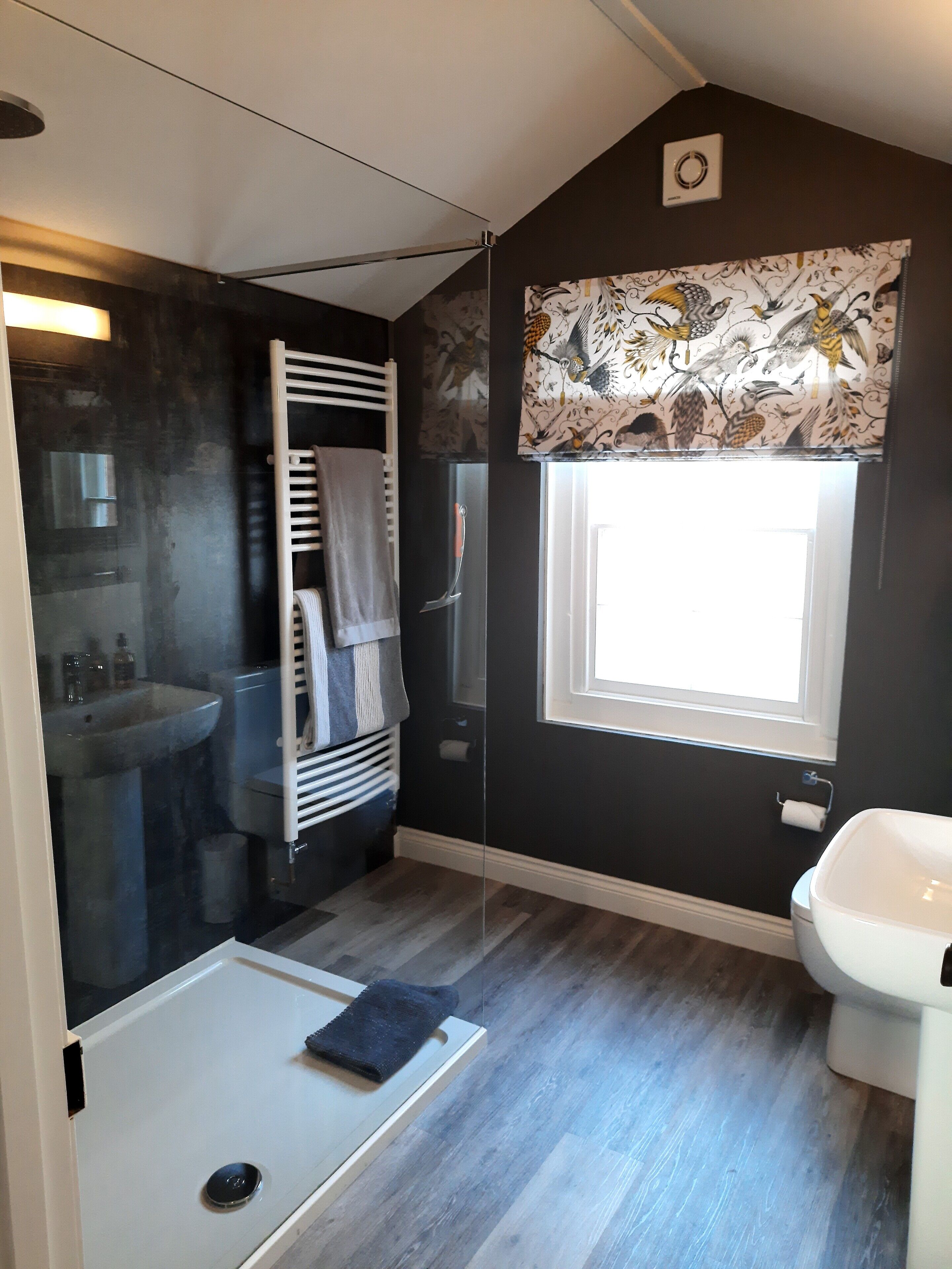 Ein Badezimmer mit Dusche, Waschbecken, Toilette und einem Fenster mit gemusterten Vorhängen.