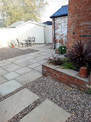 A patio area with a brick wall, a table with chairs, and a gravel pathway. - The Priory (Hereford)