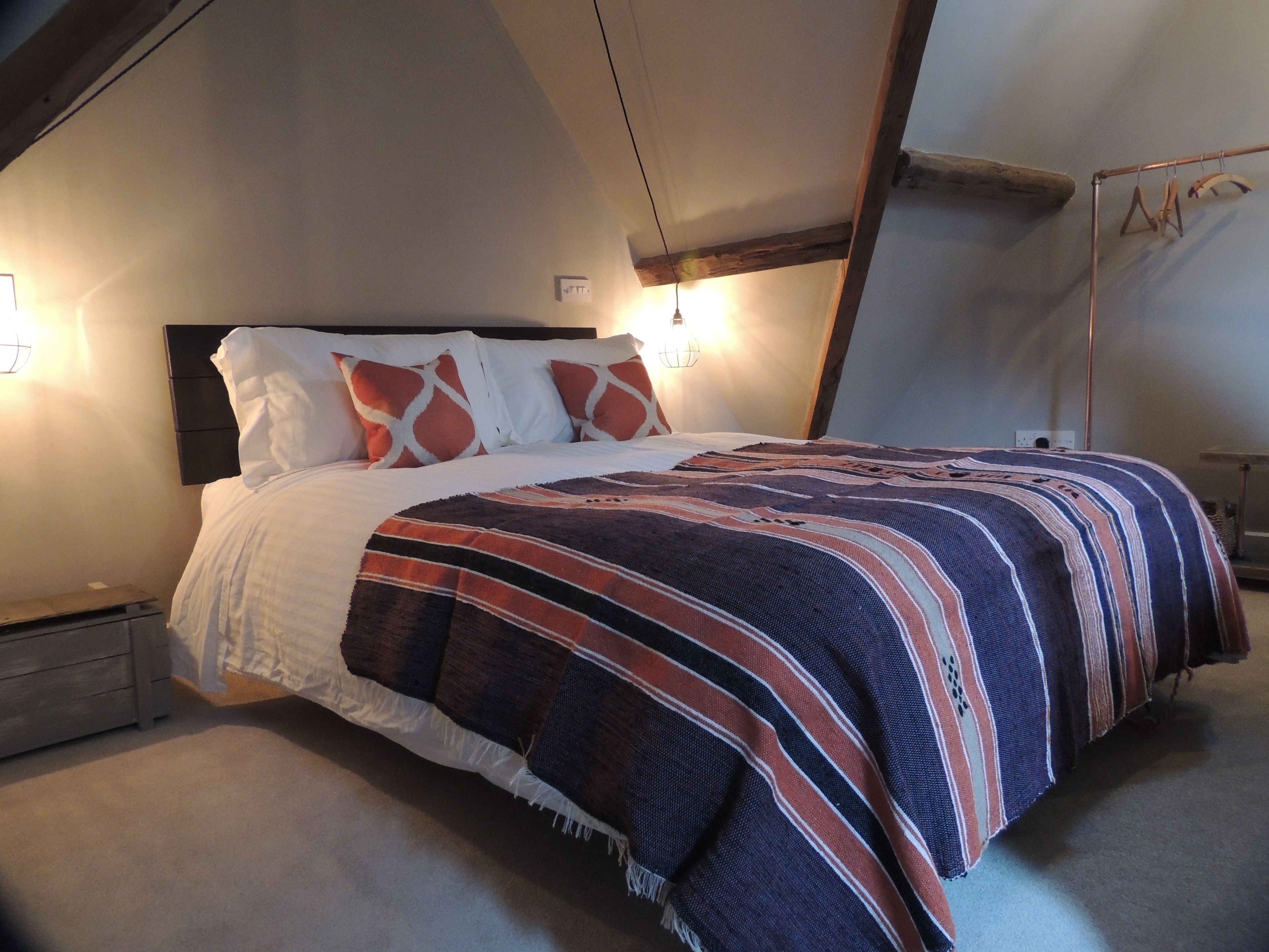 Un dormitorio con cama, mesita de noche, lámpara de pared y estructura de vigas de madera.