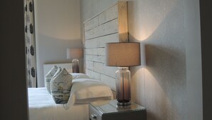 Una cama bien hecha con almohadas, una mesita de noche con una lámpara, y una pared con un diseño decorativo.