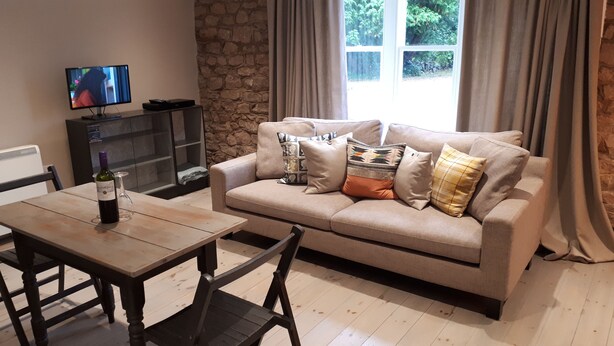 Una sala de estar con un sofá color beige, una mesa de madera, un televisor y una botella de vino.