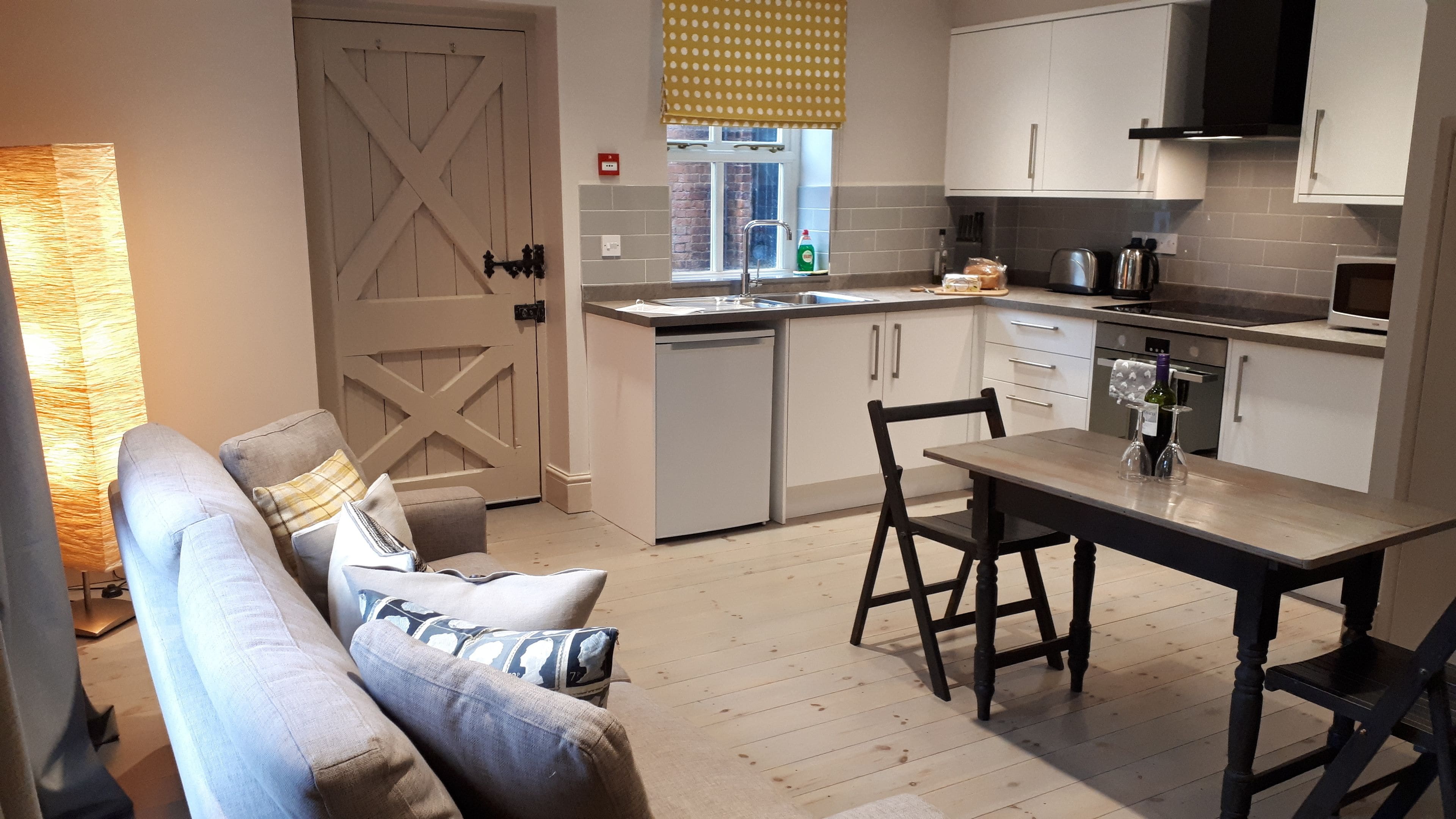 Cocina compacta con gabinetes blancos, una mesa de comedor y un sofá con cojines.