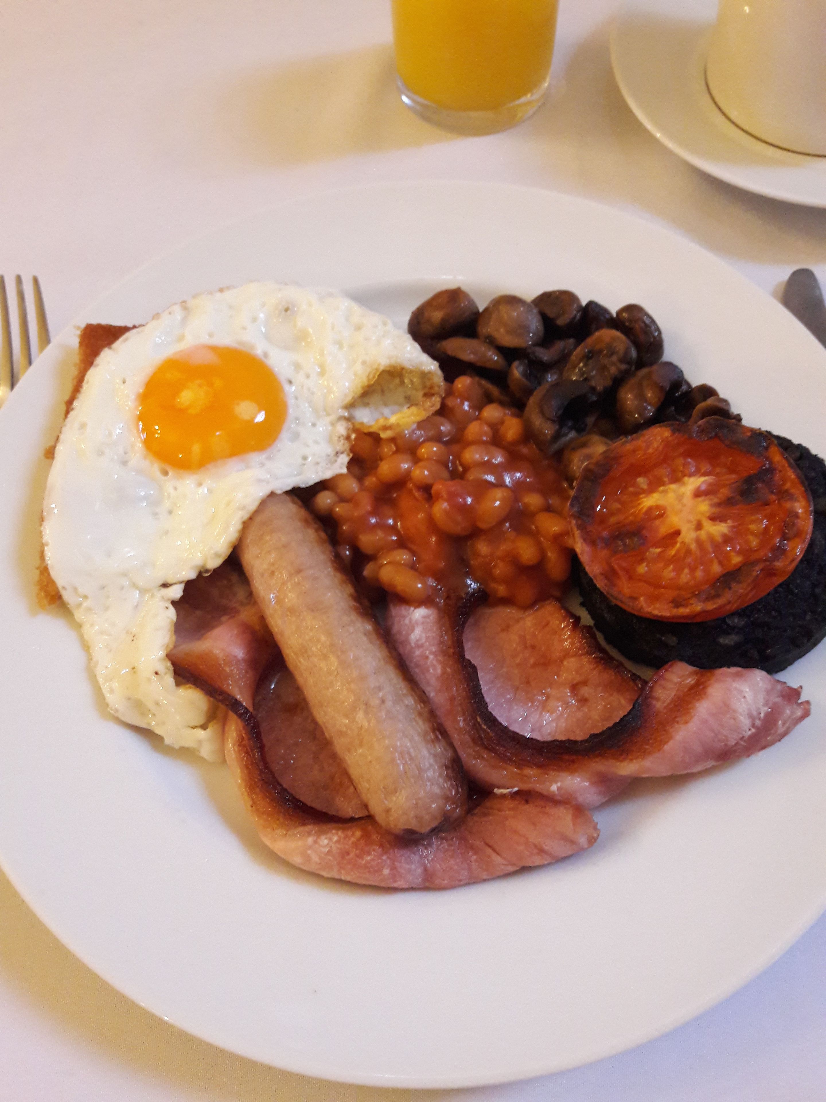 Un plato con un huevo frito, frijoles, tomates, salchichas y tocino.