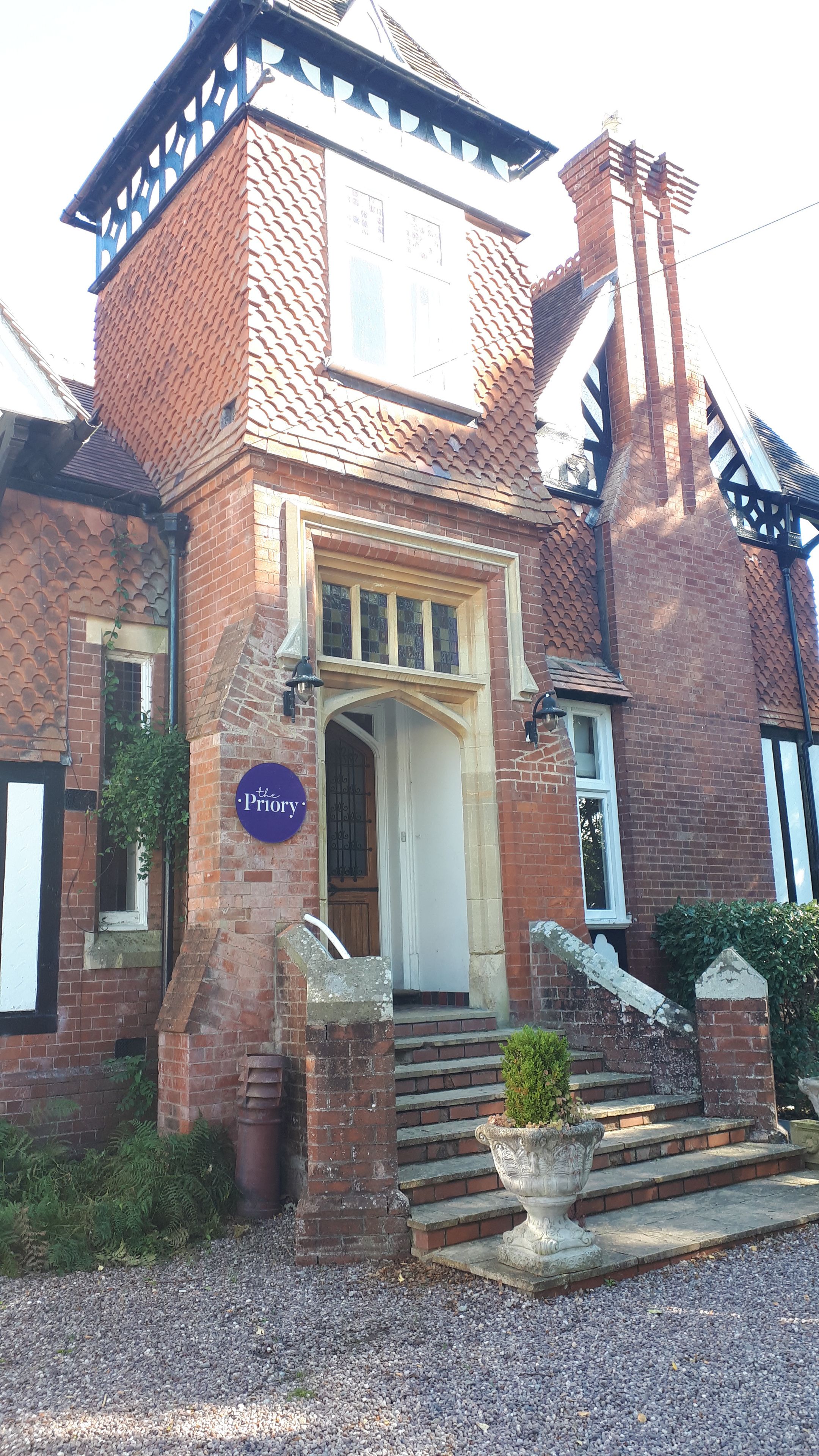A traditional brick building with a prominent entrance, a sign reading "the Priory," and a small garden area with steps leading up to the door.