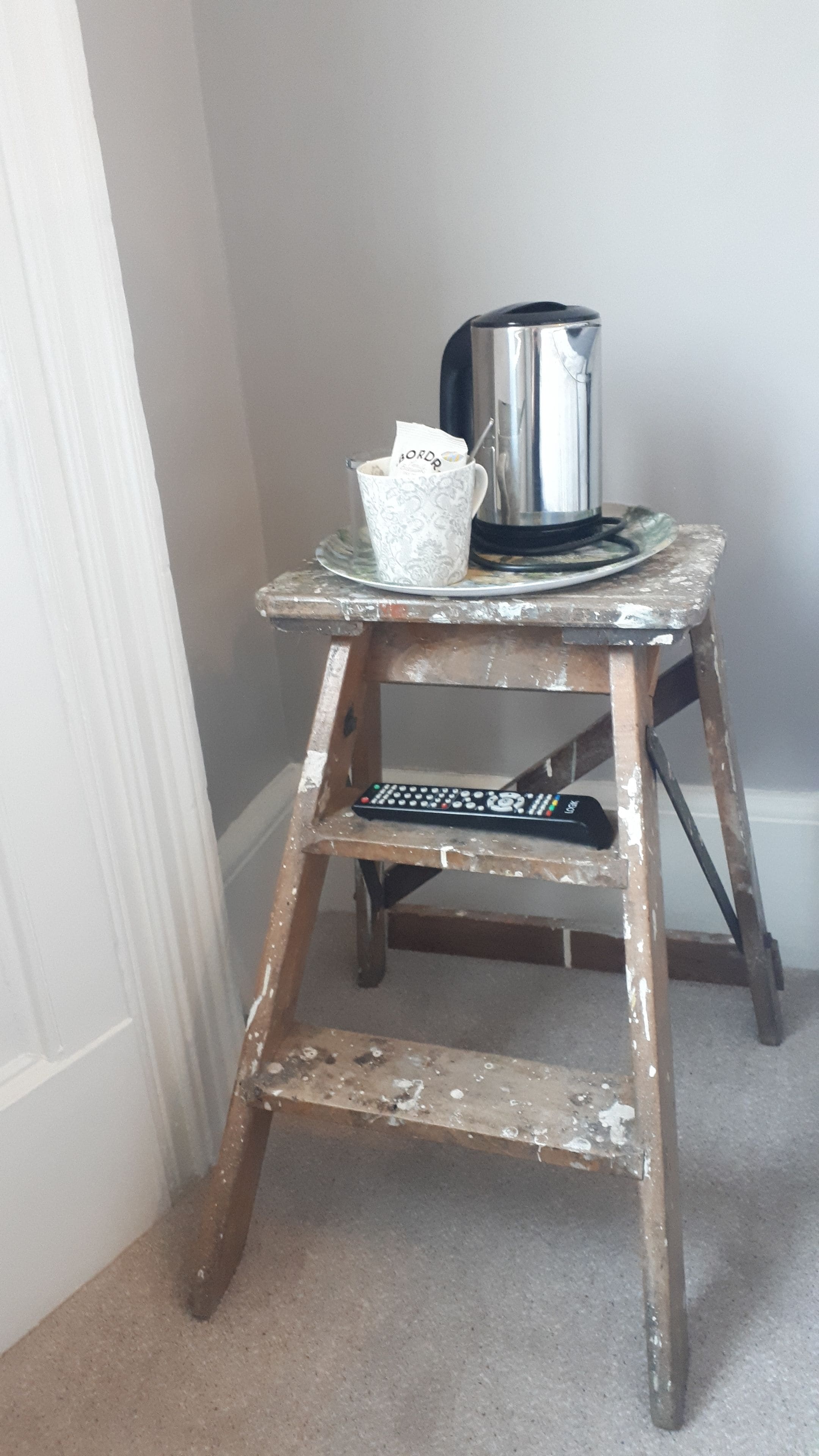 Un taburete de madera con una tetera metálica y una taza encima.