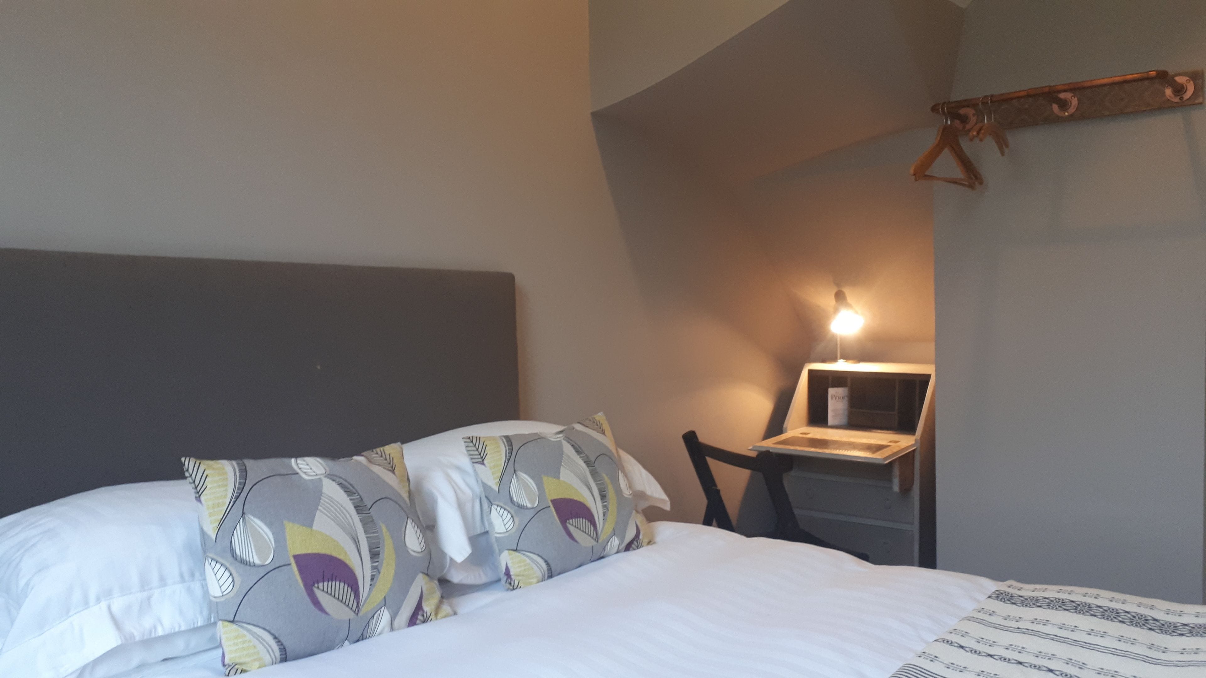 A bedroom with a bed, pillows, a desk with a lamp, and a chair.