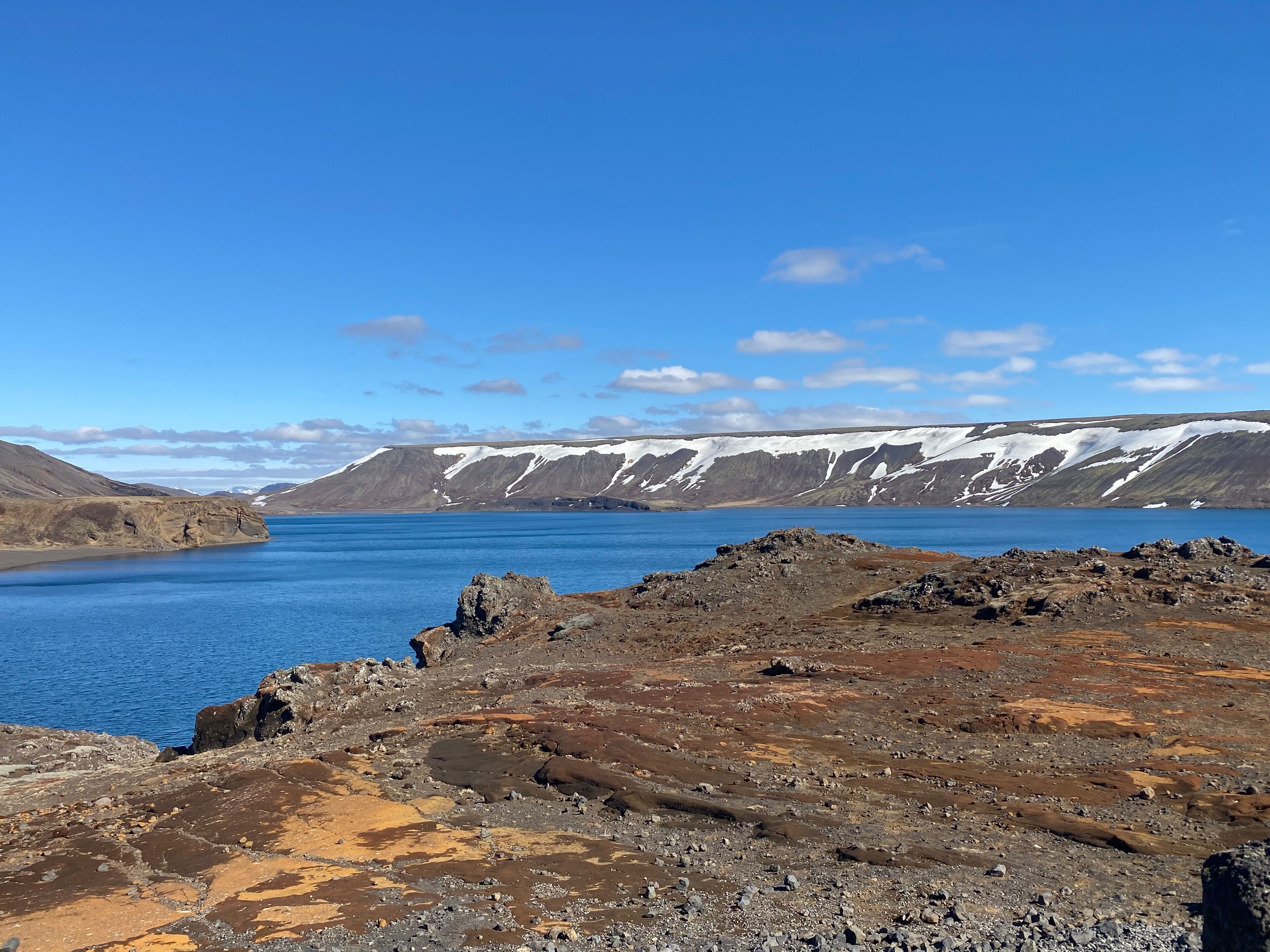 A rugged landscape with a large body of water, rocky terrain, and snow-capped mountains in the distance.