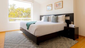 A bedroom with a bed, a nightstand, a window with a view of trees, and two framed pictures on the wall. - Capitalia | Renovated 2BR in Santa Fe’s Heart (Ciudad de México)