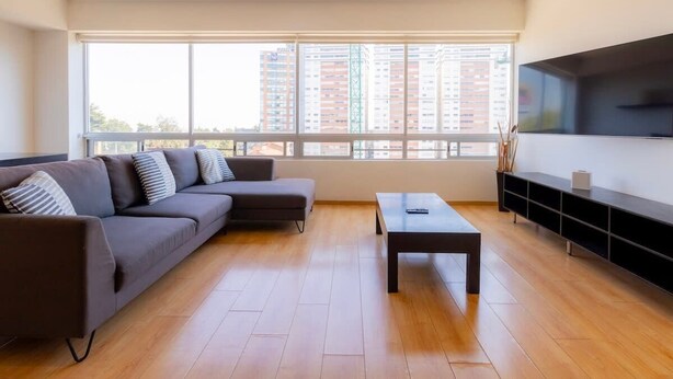 A modern living room with a sectional sofa, a coffee table, and a TV mounted on the wall. - Capitalia | Renovated 2BR in Santa Fe’s Heart (Ciudad de México)