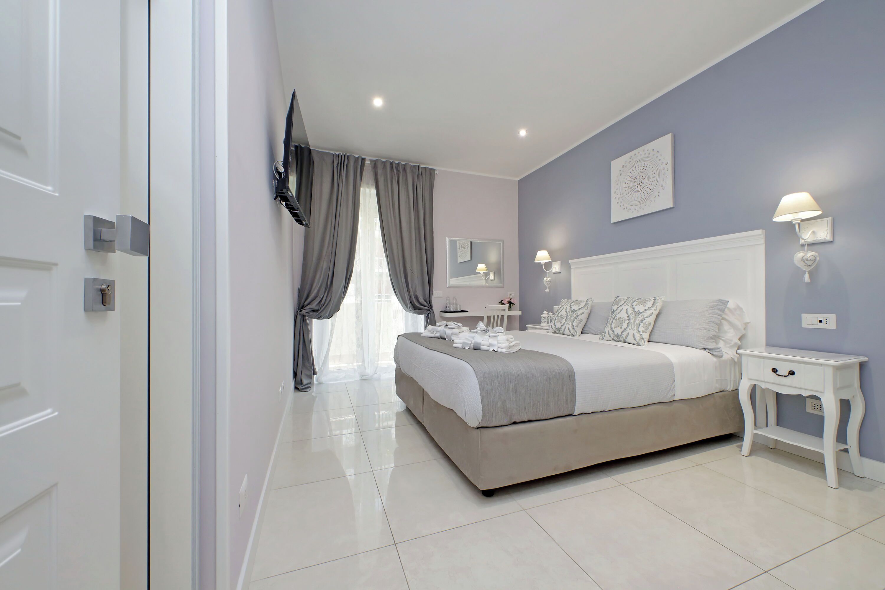 A modern bedroom with a large bed, a television mounted on the wall, and a bedside table with a lamp.