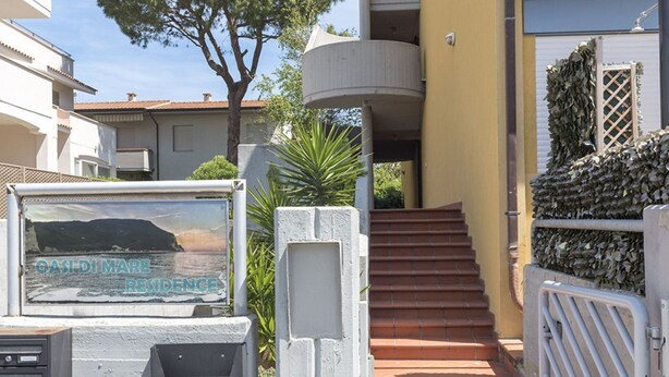 A residential building with a staircase leading to a balcony, a gate, and a signboard. - M053 - Marcelli, two-room apartment with garden 100 meters from the sea (Marcelli)