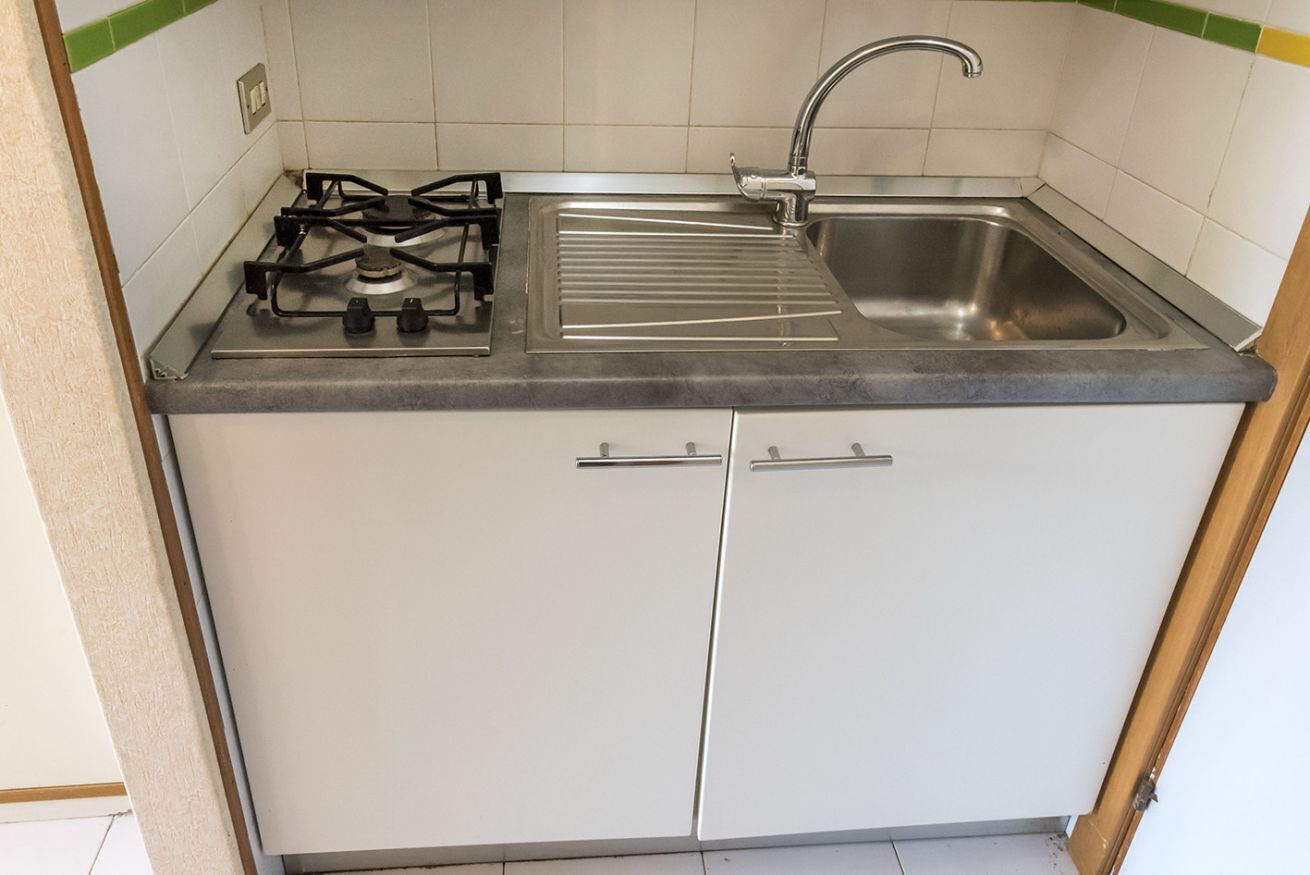 A compact kitchen with a gas stove, a sink, and two cabinets.