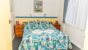 Un dormitorio con cama, dos mesitas de noche, un reloj de pared, un cuadro enmarcado y una ventana con cortinas.