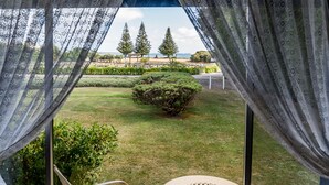 Vista desde un espacio al aire libre cubierto, con césped, un pequeño árbol y una playa a lo lejos.