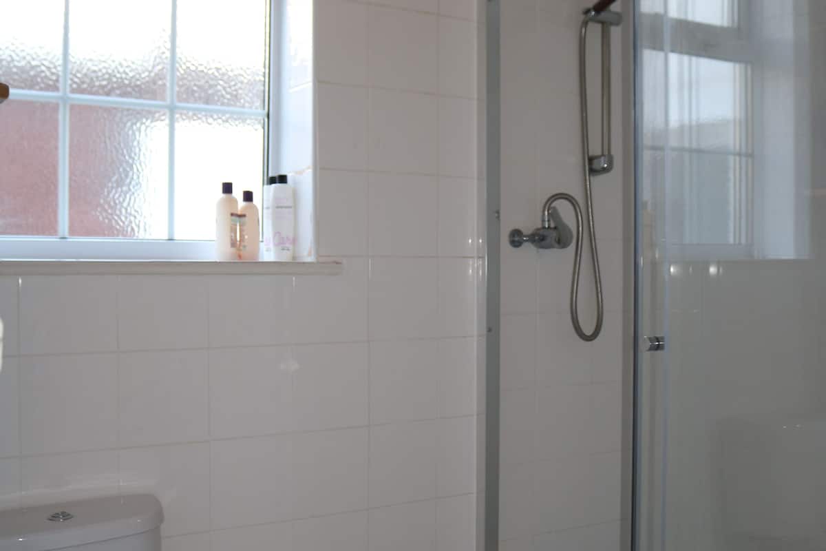 A bathroom with a toilet, a shower with a glass door, and a window above the toilet.