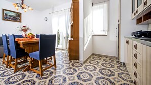 A dining area with a wooden table and blue chairs, a chandelier, and a patterned floor. - Apartment Ivo (Rovinj)