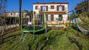 A two-story building with a balcony, surrounded by a garden with a trampoline and swing set. - Apartment Ivo (Rovinj)
