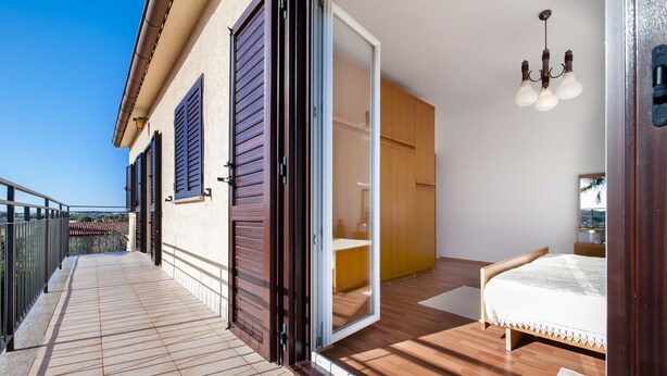 A bedroom with a wooden floor, a bed, a wardrobe, and a sliding glass door leading to a balcony. - Apartment Ivo (Rovinj)