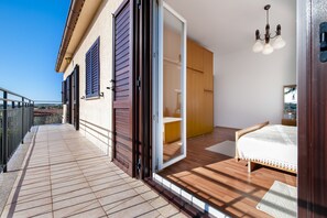 Un dormitorio con suelo de madera, una cama, un armario y un ventanal corredero que da a un balcón.