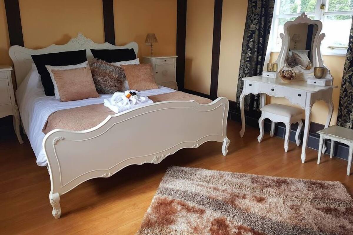 Un dormitorio con una cama grande, un tocador con espejo y un taburete pequeño.