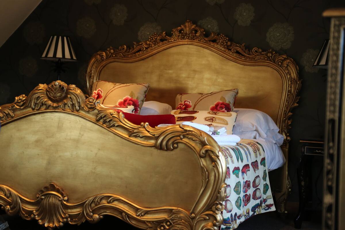 Una lujosa cama con detalles dorados ornamentales y ropa de cama con estampado floral.