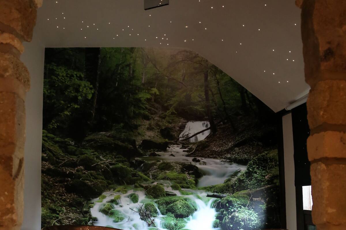 Una bañera de cobre en una habitación con paredes de piedra y un mural de una cascada en un bosque.
