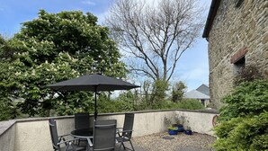 An outdoor patio with a table and chairs, a black umbrella, and a stone building in the background. - Hay Barn - Two Bedroom Cottage, Sleeps 5 (Saint Breock)
