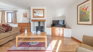 A cozy living room with a sofa, a coffee table, a fireplace, a television, and a painting. - Hay Barn - Two Bedroom Cottage, Sleeps 5 (Saint Breock)