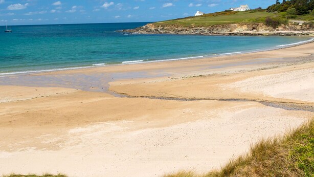 A beach with a clear view of the ocean and a grassy hill with a white building in the background. - Hay Barn - Two Bedroom Cottage, Sleeps 5 (Saint Breock)