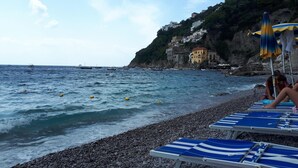 Une plage de galets avec des chaises longues bleues et une côte rocheuse.
