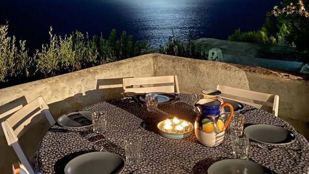Un espace extérieur aménagé pour les repas, avec une table dressée pour quatre personnes, donnant sur une étendue d’eau sous un ciel nocturne où l’on peut apercevoir la lune.