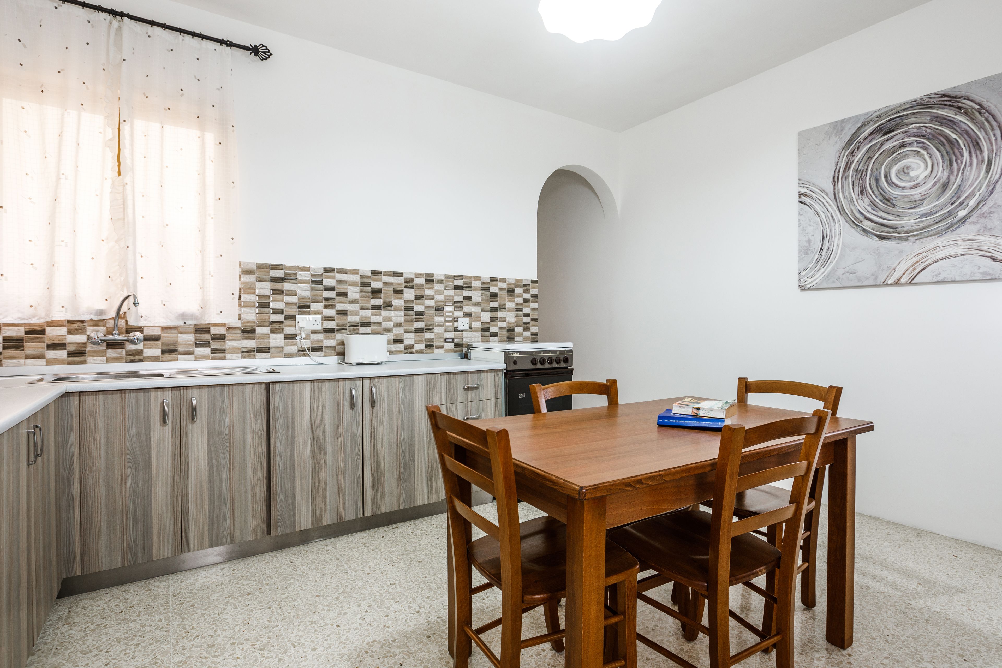 A compact kitchen with a wooden dining table and chairs, a tiled backsplash, and a modern stove.