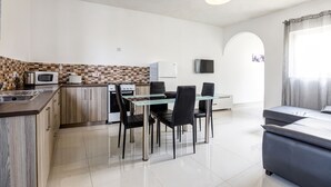A modern kitchen with a dining area, a flat-screen TV, and a sofa in a bright living space. - Dolphin Court Gozo (Zebbug)