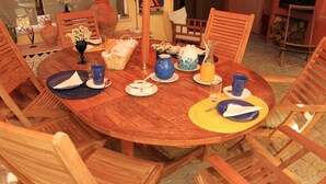 Une table ronde en bois, mise pour le repas, avec des chaises, un vase de fleurs, une carafe et un pichet.