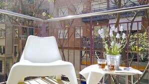 Un balcon avec une chaise en plastique blanche, une petite table sur laquelle est posée une plante en pot et deux verres contenant une boisson.