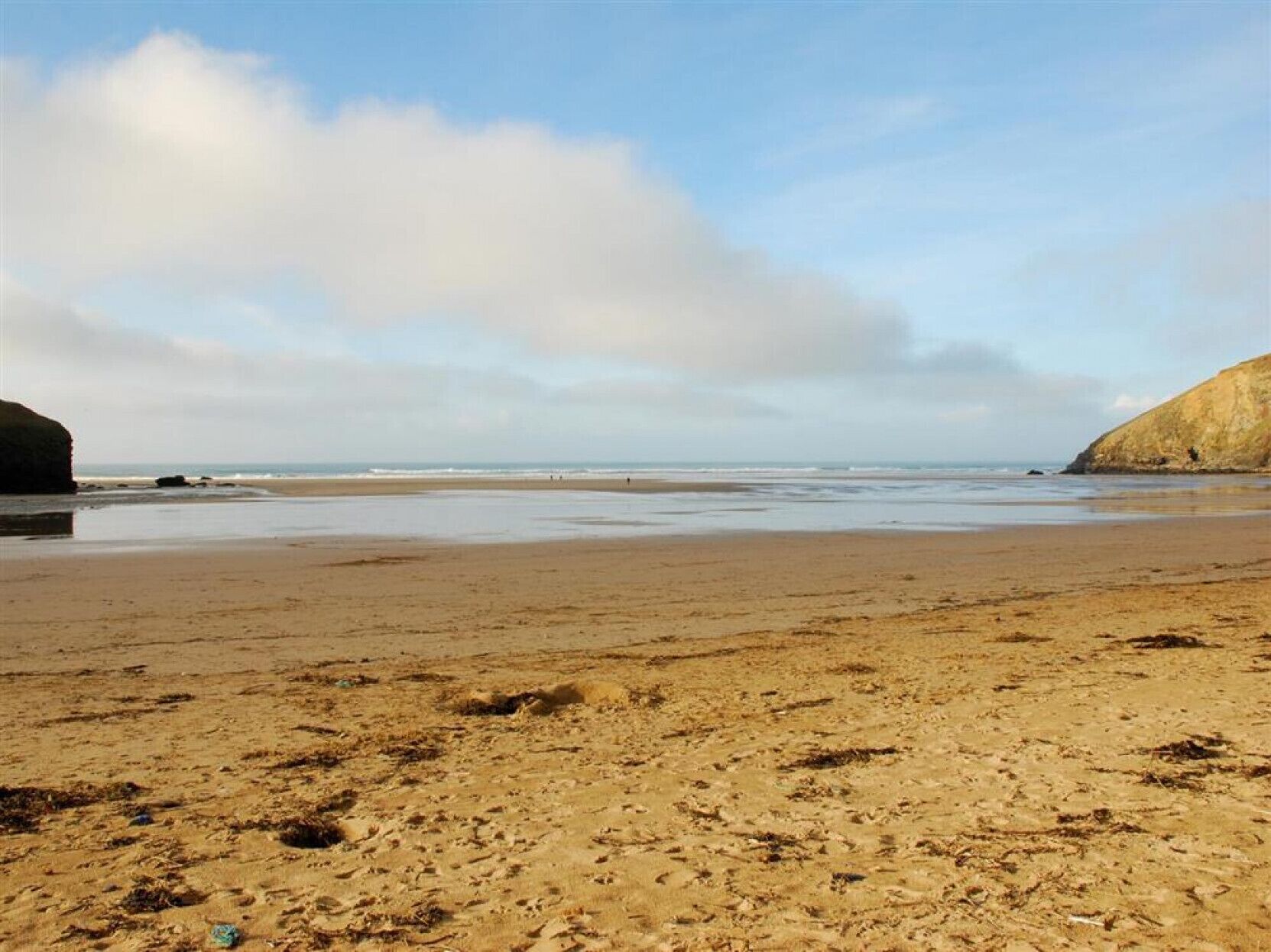 A beach with a wide sandy area, a rocky outcrop on the left, and a cliff on the right.