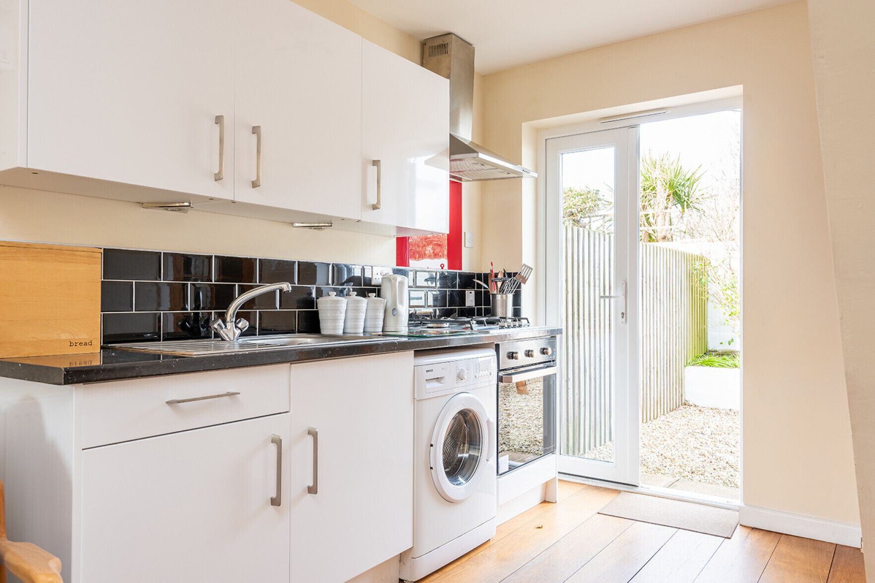 A modern kitchen with white cabinets, a black countertop, a built-in oven, and a washing machine.