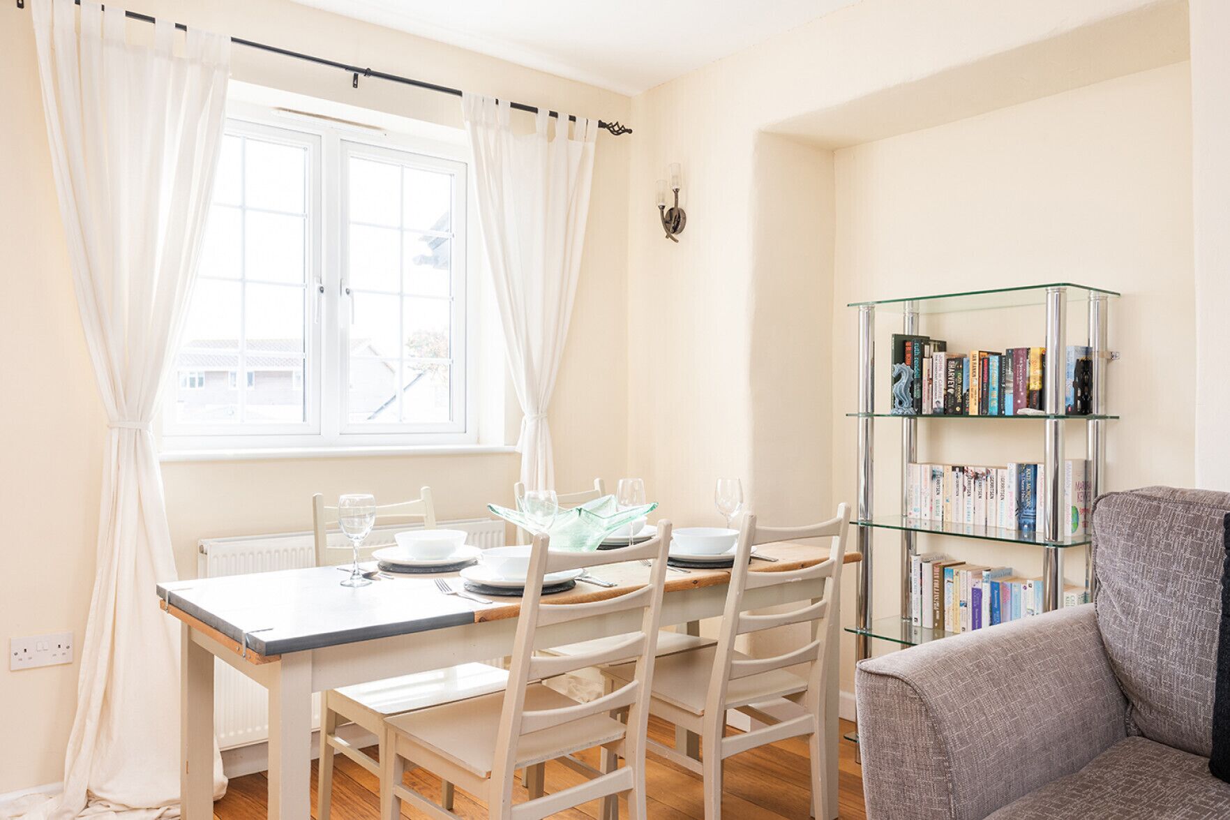 A dining area with a table set for four, a bookshelf, and a window with curtains.
