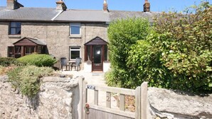 A stone house with a wooden gate, a front door, and a small patio with chairs. - Honnor Cottage - One Bedroom Cottage, Sleeps 2 (Saint Buryan)