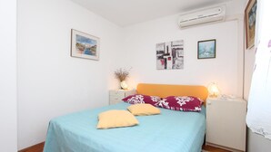 Un dormitorio con cama, mesita de noche, aire acondicionado instalado en la pared y fotografías enmarcadas.
