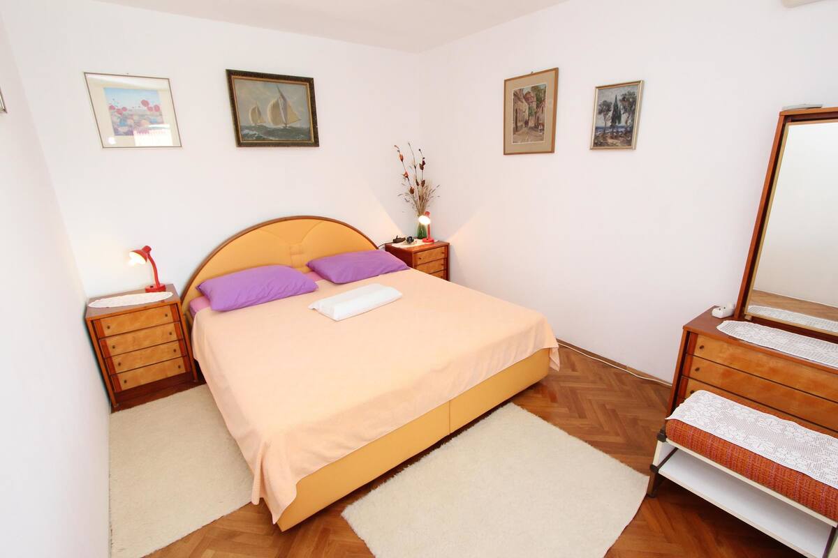 A bedroom with a bed, wooden nightstands, a dresser, a mirror, and wall-mounted artwork.
